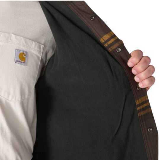 Close-up of a person wearing a Carhartt shirt, opening the collar to show a dark charcoal inner layer or underlayer. The right sleeve shows a beige cuff with brown and gold stripes, and the left chest pocket displays the Carhartt logo.