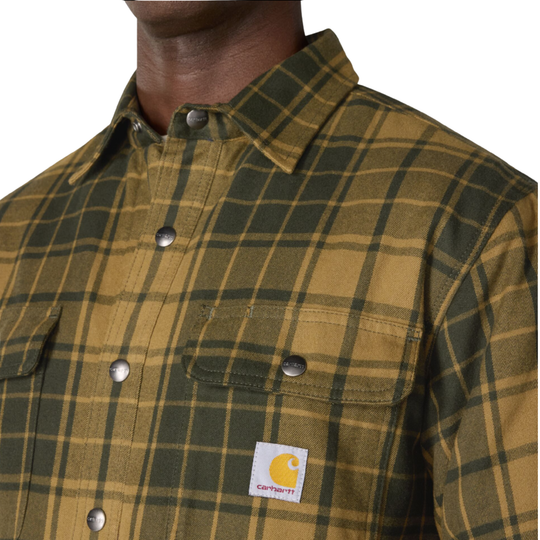 Close-up of a man wearing a Carhartt plaid button-up shirt in olive green and tan, showing the collar, chest pockets, and Carhartt logo patch.
