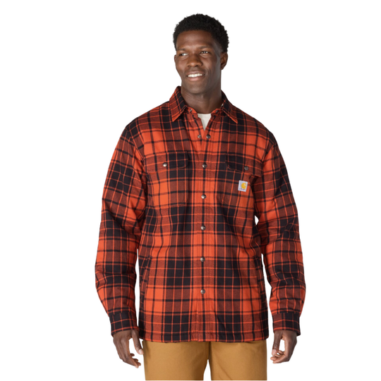 A man wearing a red and black plaid Carhartt button-down shirt, paired with tan pants, standing against a plain white background.