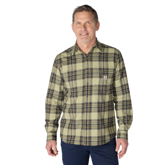 A man wearing a long-sleeve plaid button-up shirt in olive green and beige with dark brown lines, paired with navy pants, against a plain white background.