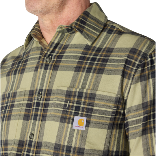 Close-up of a man wearing a Carhartt plaid button-up shirt in olive green, beige, and navy. The shirt features a classic plaid pattern and the signature Carhartt brand patch on the chest pocket.