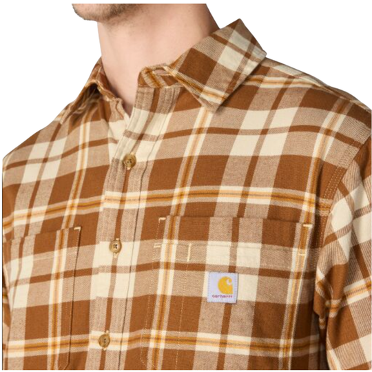 A close-up of a man wearing a Carhartt plaid button-up shirt in brown and cream. The shirt features a classic check pattern, a button-down front, and the signature Carhartt brand patch on the chest pocket.