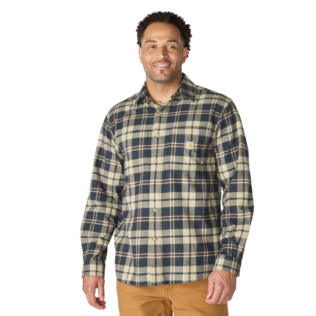 A man wearing a Carhartt long-sleeve plaid button-up shirt in navy blue and beige, paired with tan pants, against a plain white background.