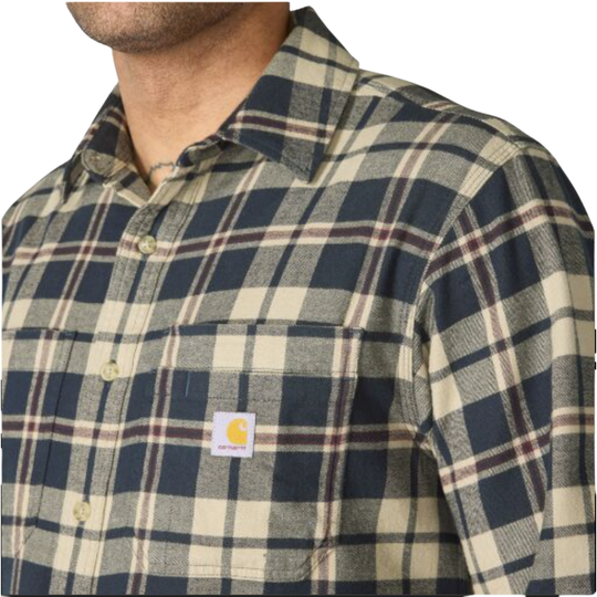 Close-up of a man wearing a Carhartt plaid button-down shirt. The shirt features a navy blue, beige, and brown plaid pattern with a visible Carhartt logo patch on the chest pocket.