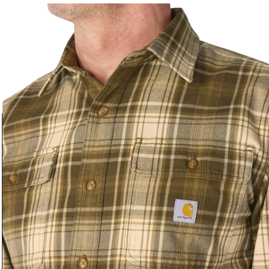 Close-up of a man wearing a Carhartt plaid button-down shirt in olive green and beige, showing the collar, buttons, and the Carhartt logo patch on the chest pocket.