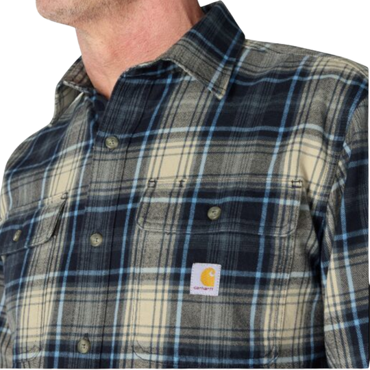 Close-up of a man wearing a Carhartt plaid button-up shirt. The shirt features a pattern of navy blue, beige, and light blue, with two chest pockets and a visible Carhartt logo patch on the left chest.