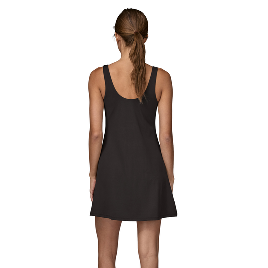 A woman viewed from the back wearing a sleeveless black mini dress with a wide scoop neckline and flared skirt, set against a plain white background.