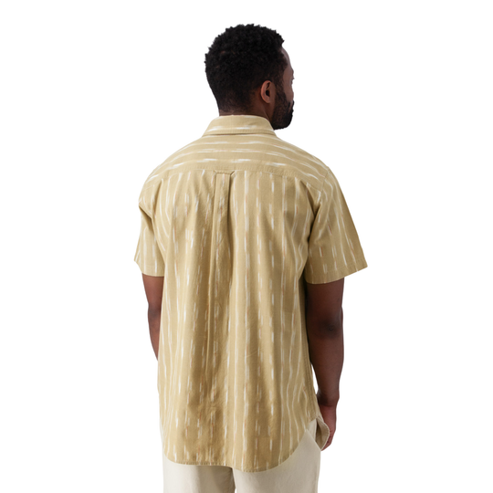 A man viewed from the back wearing a short-sleeve button-up shirt with a beige and white vertical ikat stripe pattern, paired with light beige pants, against a solid white background.