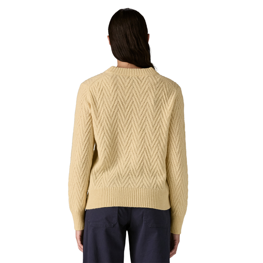 Person wearing a beige cable knit sweater on a white background