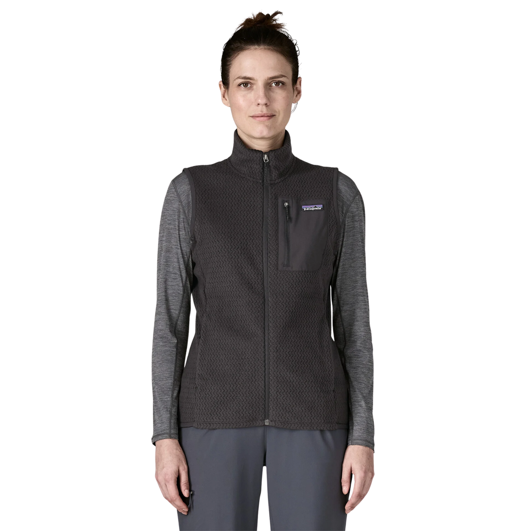 A woman modeling a dark gray Patagonia fleece vest over a heather gray long-sleeve shirt and gray pants, shown against a plain white background.