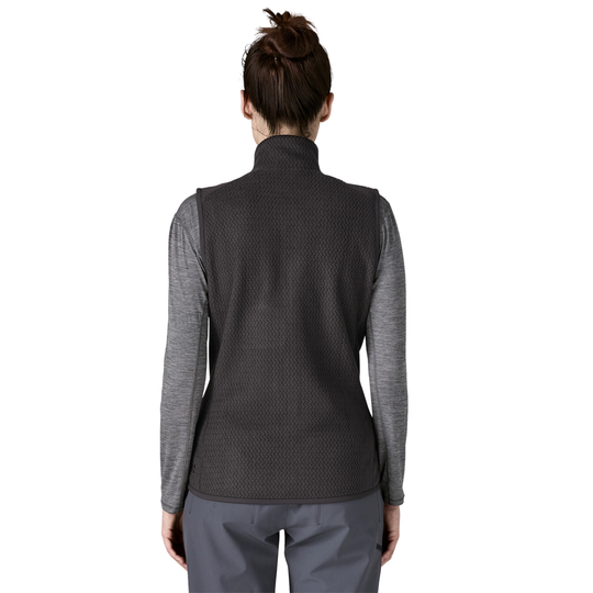 A woman viewed from the back wearing a dark charcoal gray textured sleeveless vest over a heather gray long-sleeve shirt, paired with gray pants, against a plain white background.