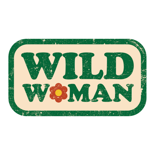 A rectangular vintage-style sticker or sign with rounded corners, featuring the words “WILD WOMAN” in dark green block letters on a cream background, with a small red flower replacing the O in “WOMAN.”.