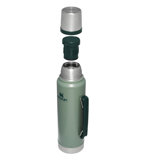 A Stanley vacuum-insulated water bottle in sage green with a dark green carrying loop and silver metal accents, shown with its lid components disassembled vertically above the bottle on a white background.