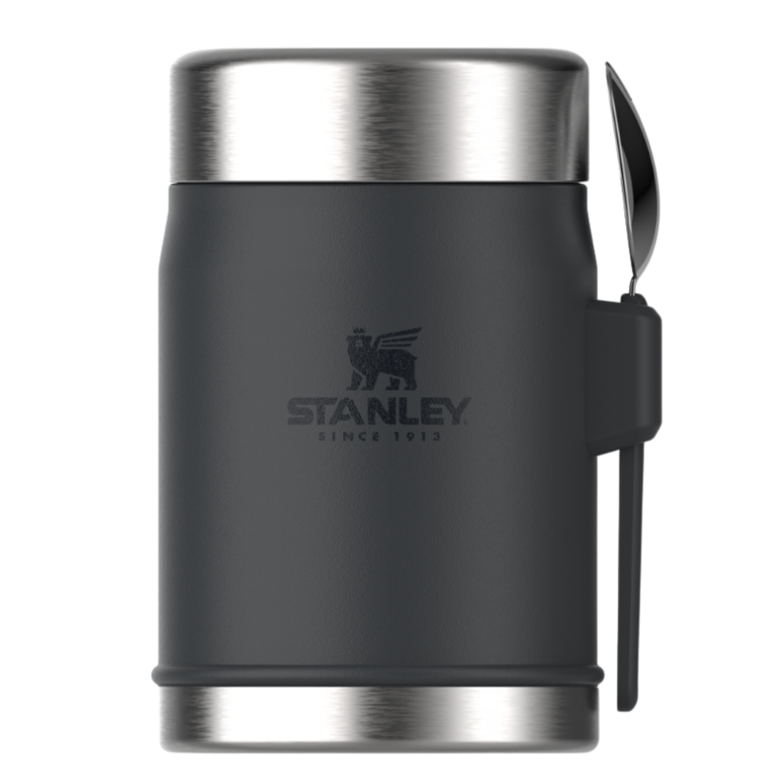 Stanley insulated container in dark gray with a stainless steel lid and base, featuring a black silicone strap with a spoon attached, on a white background.