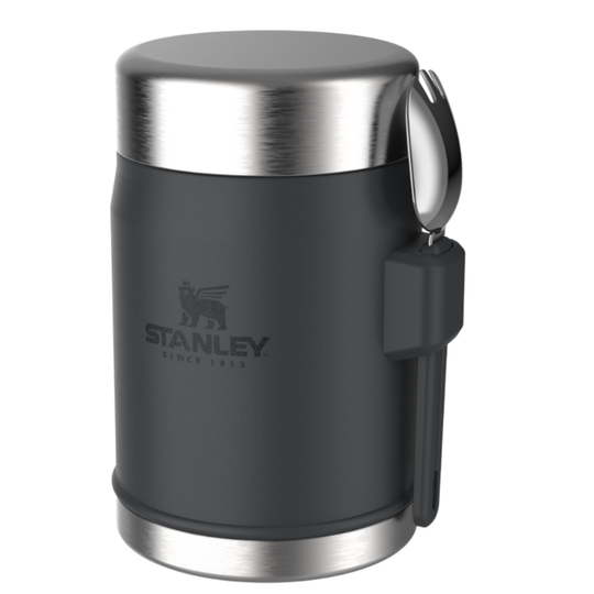 A dark gray Stanley vacuum-insulated can cooler with a brushed stainless steel lid and base, featuring a black carrying handle and the embossed Stanley logo on the front.