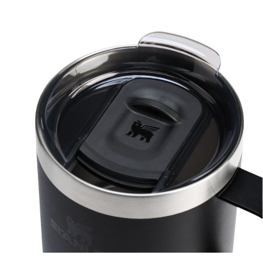 Close-up of a black travel tumbler with a stainless steel rim and a clear flip-top lid, showing a black logo on the lid and a faint logo on the tumbler body.
