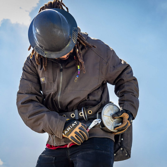 Person wearing a helmet and gloves holding a tool against a blue sky.