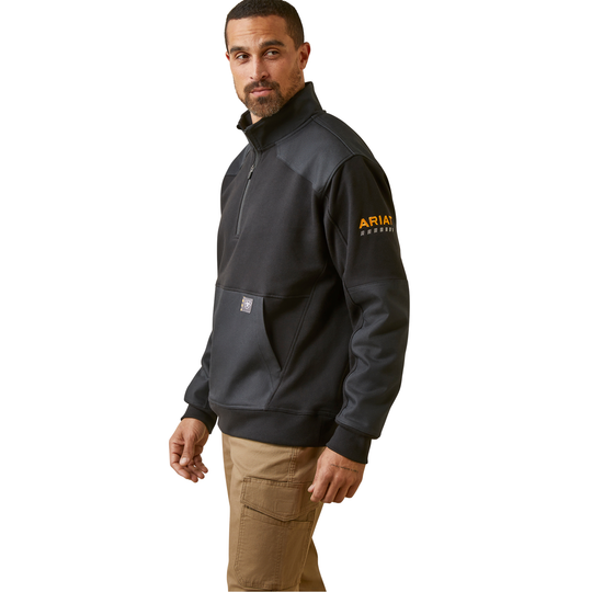 A man wearing a black and dark gray quarter-zip pullover jacket with a visible 'Ariat' logo on the left sleeve, paired with khaki cargo pants, against a plain white background.