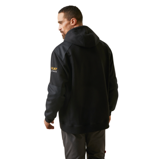 Man wearing a black jacket with a brand logo on the back, standing against a white background