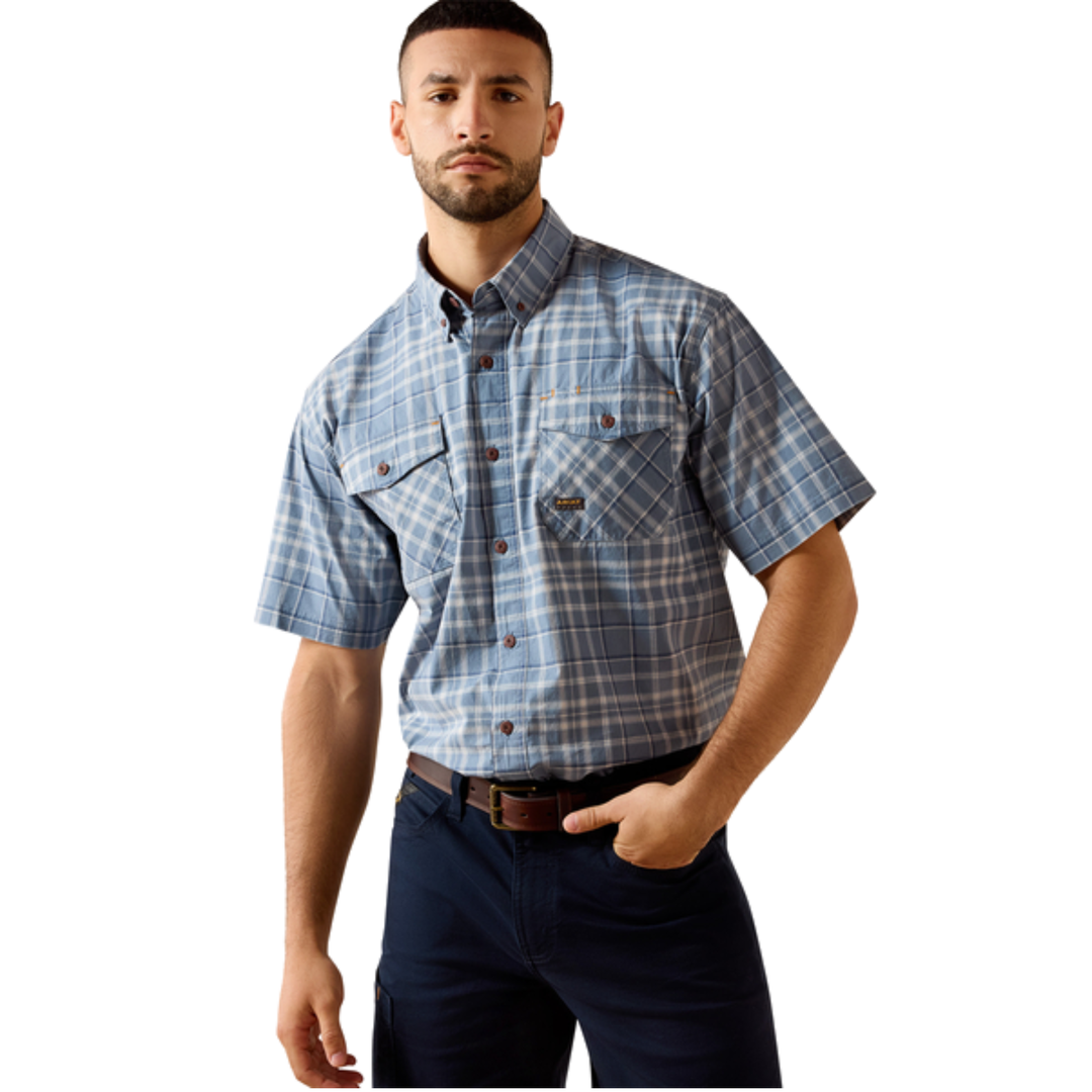 A man wearing a short-sleeve button-up plaid shirt in blue and white, paired with dark navy pants, against a plain white background.