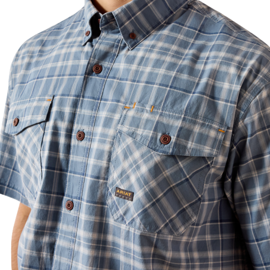 Close-up of a short-sleeve button-up shirt with a blue, white, and light gray plaid pattern. The shirt features brown buttons and a chest pocket with a visible NAT brand label.