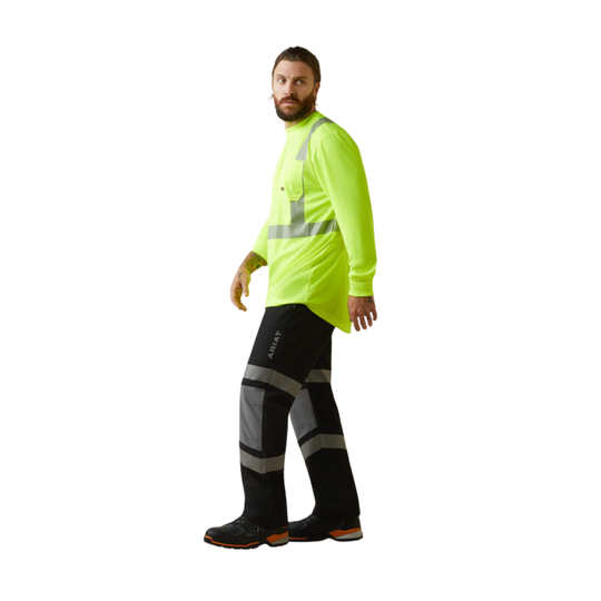 A man wearing a bright neon yellow-green long-sleeve high-visibility work shirt with reflective silver stripes and black high-visibility trousers with reflective knee and lower-leg panels, standing against a plain white background.
