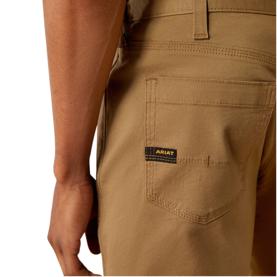Close-up of a person wearing tan work pants, showing the back pocket with a visible Ariat brand tab and part of the leg and hand.