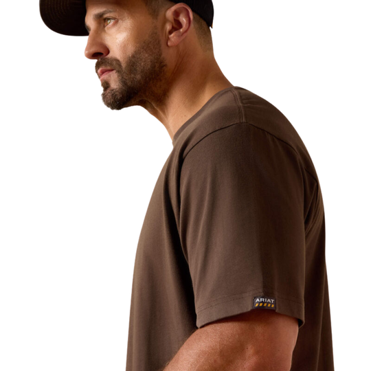 A man in profile wearing a dark brown short-sleeve crewneck t-shirt and a black baseball cap. The shirt has a small 'ARTIST REACT' logo patch on the left sleeve cuff, set against a plain white background.