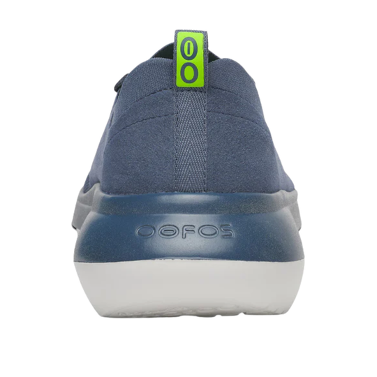 A rear view of a blue slip-on shoe with a white sole and a bright green pull tab featuring the number '00'. The brand name 'OOFOS' is embossed on the heel.