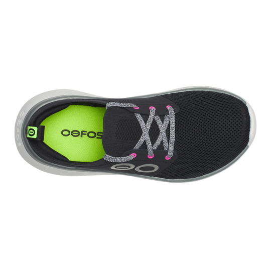 A single OOFOS slip-on sneaker shown from a top-down view. The shoe features a black mesh upper, glittery silver laces with pink tips, a gray translucent sole, and a bright neon green inner lining with the OOFOS brand name printed in black.