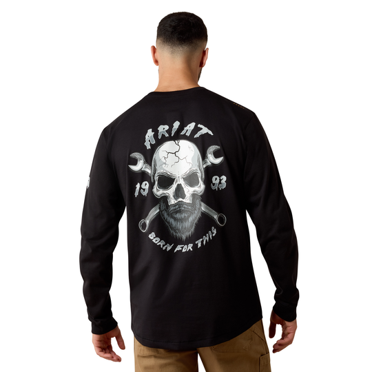 A man viewed from the back wearing a black long-sleeve t-shirt with a large white graphic on the back featuring a skull, wrenches, and the text 'ARIAT' and 'BORN FOR THIS'.