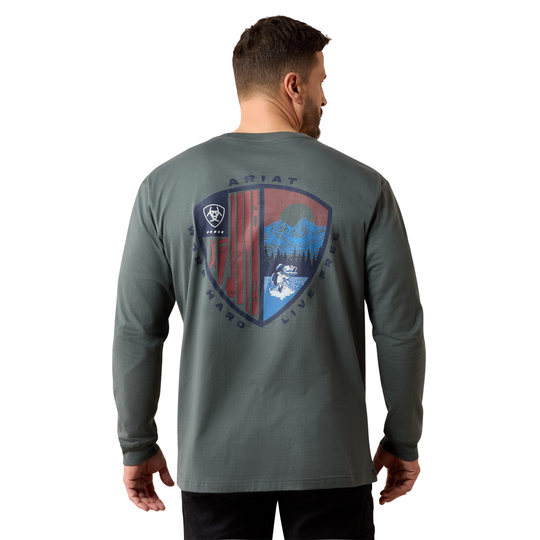 A man viewed from the back wearing a dark gray long-sleeve t-shirt with a large shield graphic on the back featuring red, blue, and white elements, and the brand name ARIAT.