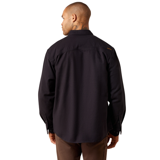 A man viewed from the back wearing a dark long-sleeve button-up shirt and brown pants against a plain white background.