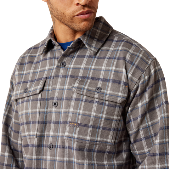 A close-up of a man wearing a gray and blue plaid button-down shirt with two chest pockets, photographed against a plain white background.