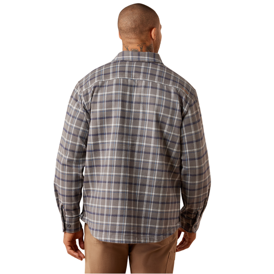 A man viewed from behind wearing a long-sleeve plaid button-up shirt in gray, white, and blue, paired with tan pants, against a plain white background.