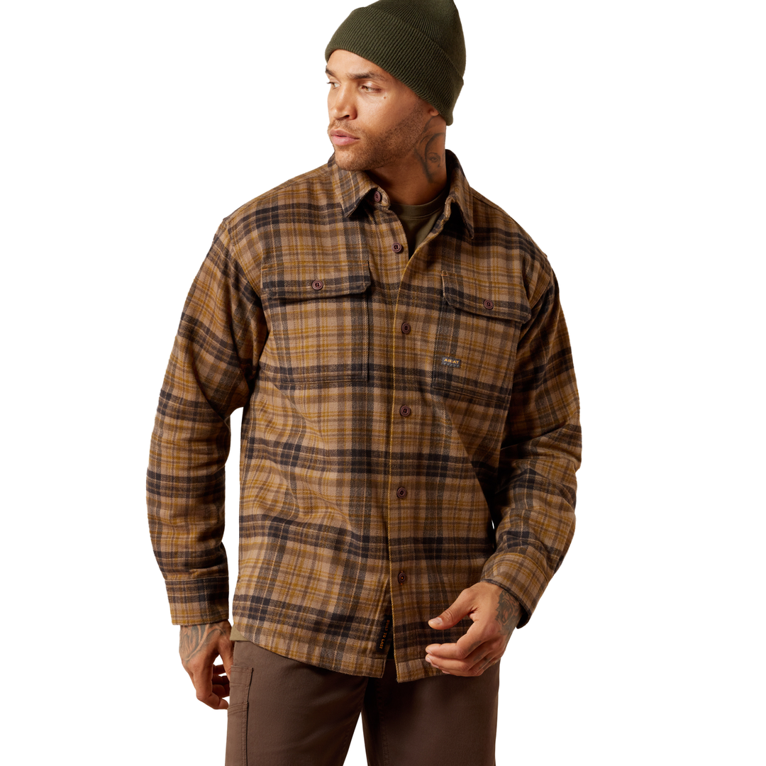 A man wearing a brown and tan plaid button-up shirt jacket, a dark green beanie, and brown pants, photographed against a plain white background.