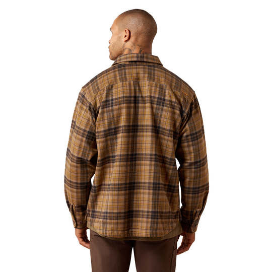 A man viewed from the back wearing a brown and tan plaid flannel shirt, paired with dark brown pants, against a solid white background.