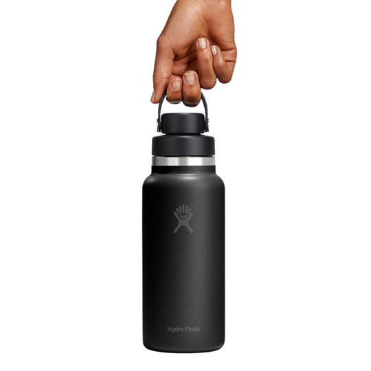 A matte black HydroFlask water bottle with a black lid and handle, held by a hand against a solid white background.