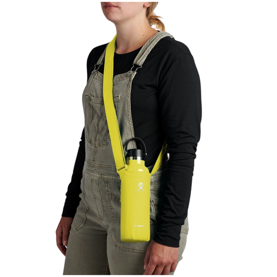 A woman wearing gray denim overalls and a black long-sleeve shirt models a bright yellow insulated water bottle carrier bag with a matching yellow shoulder strap, holding a yellow water bottle.