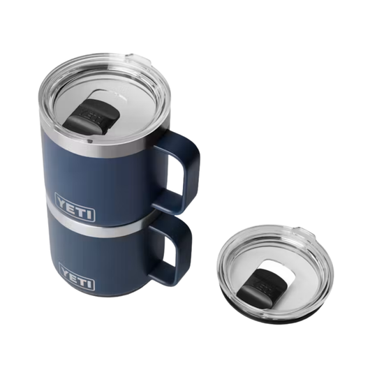 Two stacked YETI insulated tumblers in navy blue with silver trim and clear lids, shown on a white background with one lid placed beside the tumblers.