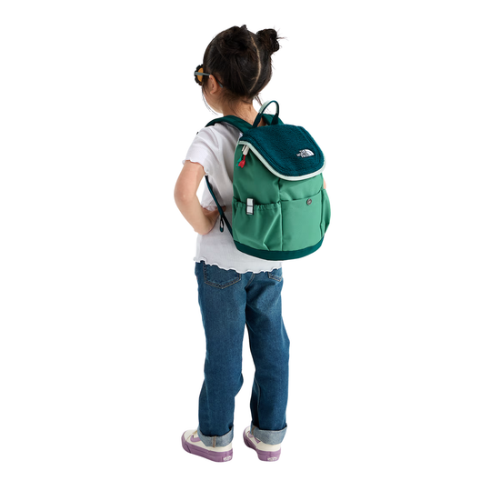A child wearing a white t-shirt, blue jeans, and sneakers, shown from behind while wearing a green and teal backpack. The backpack features a white embroidered logo on the top right that reads 'THE NORTH FACE'.