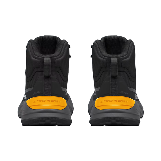 A pair of black mid-height outdoor boots shown from the back, featuring a prominent bright yellow heel accent and a dark gray sole.