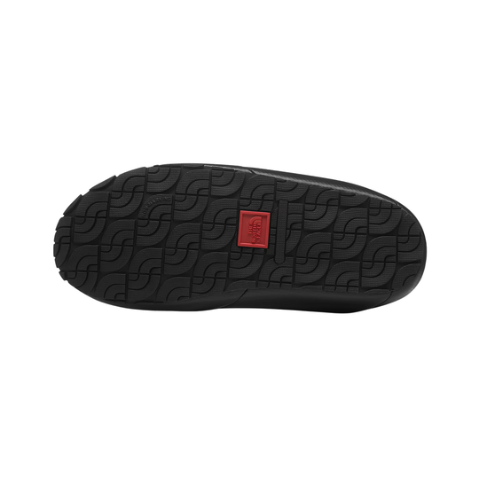 The black rubber outsole of a shoe, featuring a textured geometric pattern and a small red square logo patch in the center, shown against a plain white background.
