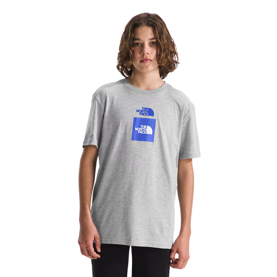 A young man wearing a heather gray t-shirt with a blue graphic on the chest, paired with black pants, against a plain white background.