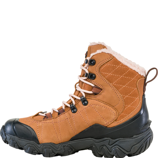 A mid-height lace-up hiking boot in tan suede and synthetic fabric, featuring a black rugged sole, black toe cap, black lace hardware, and a white faux-fur lining visible at the collar.