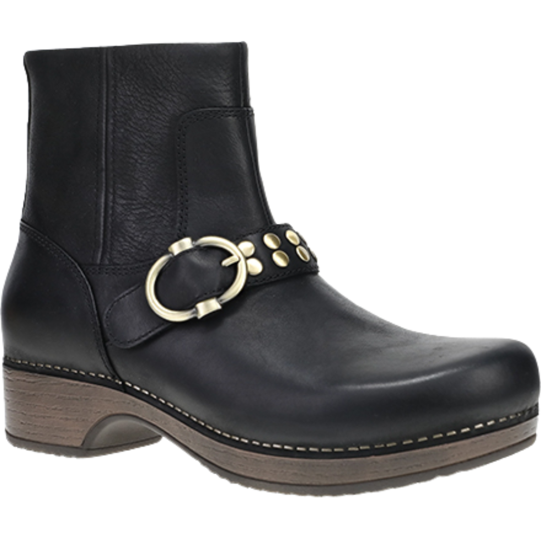 A black leather ankle boot with a brown stacked wood-look heel and sole, featuring a decorative strap across the instep with a large gold-tone ring buckle and small gold studs.