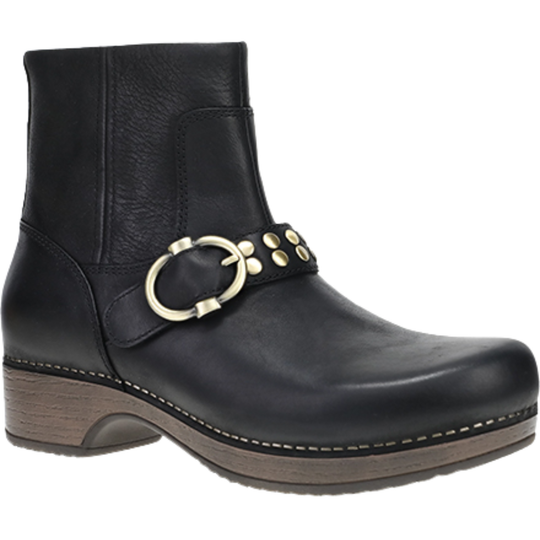 A black leather ankle boot with a brown stacked wood-look heel and sole, featuring a decorative strap across the instep with a large gold-tone ring buckle and small gold studs.