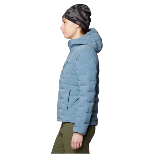 A side profile view of a person wearing a light blue hooded puffer jacket, a dark gray and black patterned beanie, and olive green pants, set against a plain white background.