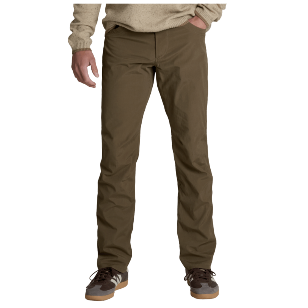 A person wearing olive brown pants, a beige sweater, and brown sneakers with white stripes, shown from the waist down against a plain white background.