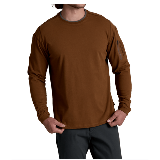 A man wearing a brown long-sleeve performance shirt with a dark gray crew neck collar and dark gray pants, shown from the chin down against a white background.